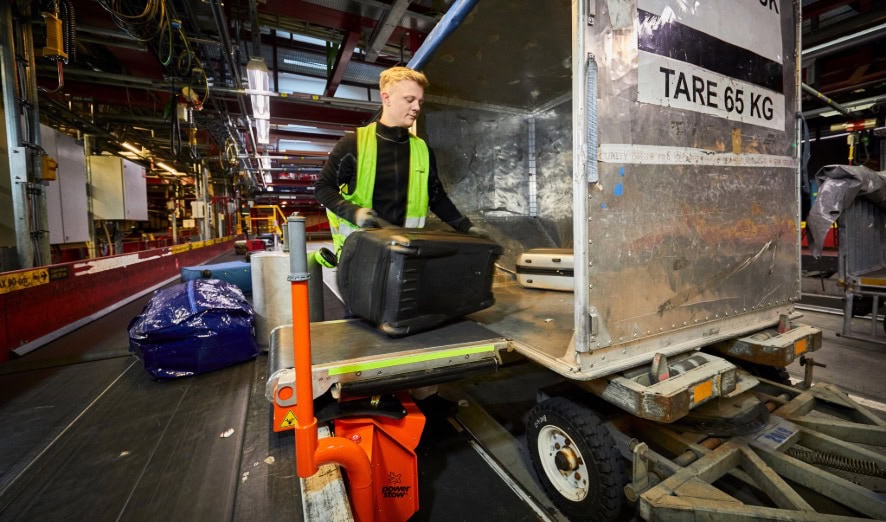 Ground handler using Power Stow Transfer Belt to unload baggage from ULD container