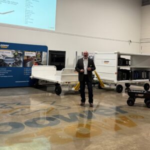 One presenter speaking to a seated audience at a corporate event in an industrial warehouse setting, with Power Stow logo on the floor